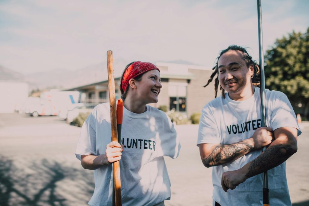 Two cheerful volunteers with tools, working outdoors for community service, promoting charity work.